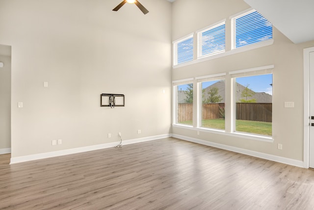 unfurnished living room with a towering ceiling, light hardwood / wood-style floors, and ceiling fan