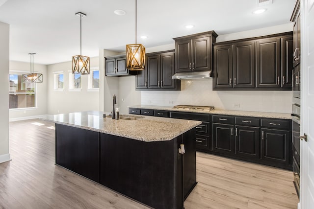 kitchen featuring sink, stainless steel gas cooktop, decorative light fixtures, a kitchen island with sink, and light hardwood / wood-style floors