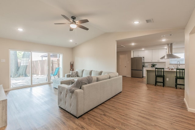 living area with light wood finished floors, ceiling fan, visible vents, and vaulted ceiling