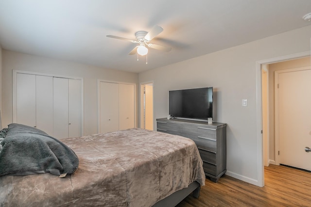 bedroom featuring baseboards, wood finished floors, a ceiling fan, and multiple closets