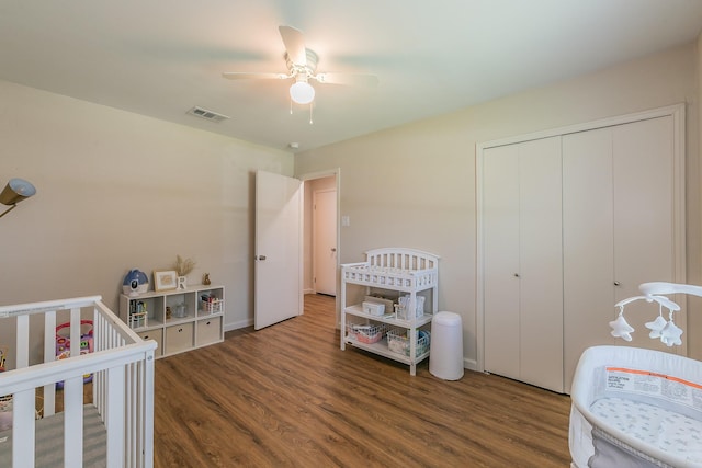 bedroom with dark wood-style floors, a crib, a closet, and visible vents