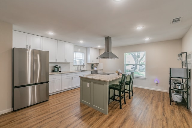 kitchen featuring stainless steel fridge, a kitchen island, plenty of natural light, white cabinetry, and exhaust hood