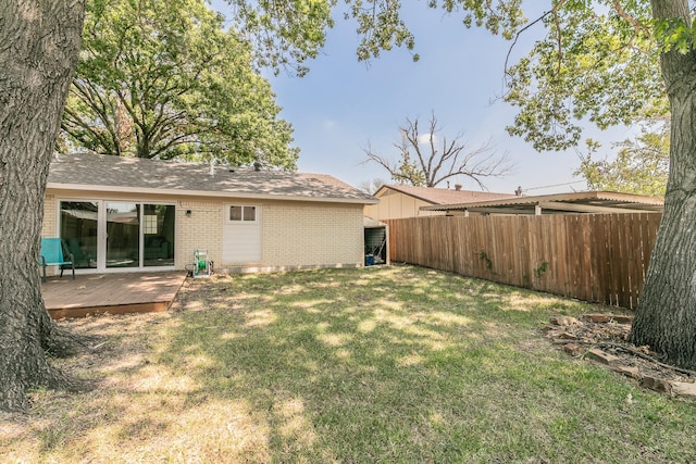 rear view of house with brick siding, a yard, a wooden deck, and fence