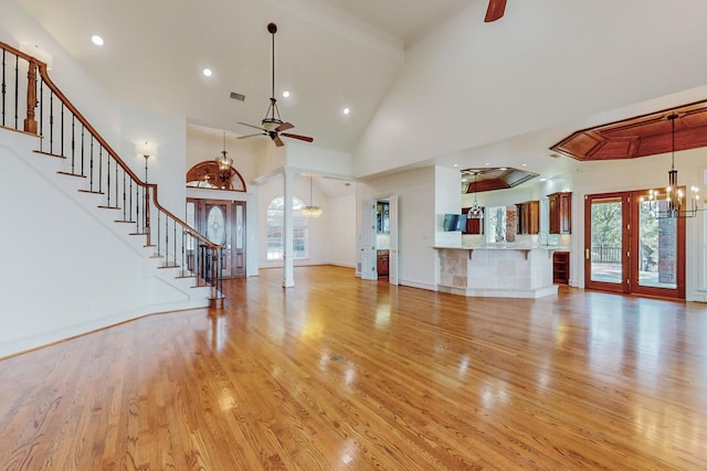 unfurnished living room with french doors, ceiling fan with notable chandelier, high vaulted ceiling, and light hardwood / wood-style flooring