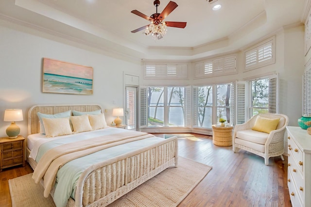 bedroom with ceiling fan, a tray ceiling, crown molding, and hardwood / wood-style floors