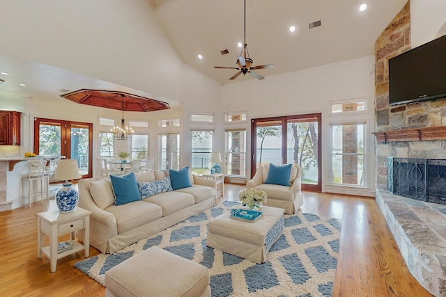 living room featuring ceiling fan with notable chandelier, high vaulted ceiling, a fireplace, and light hardwood / wood-style floors