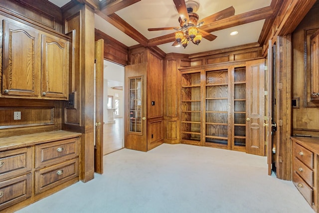 carpeted office space featuring ceiling fan, beamed ceiling, wooden walls, and crown molding