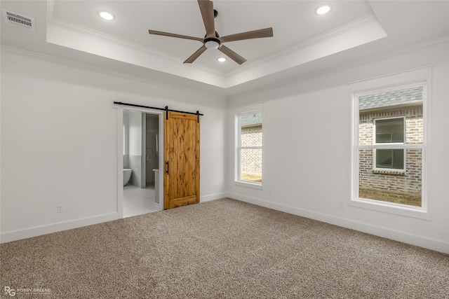 empty room featuring a barn door, carpet flooring, and a tray ceiling