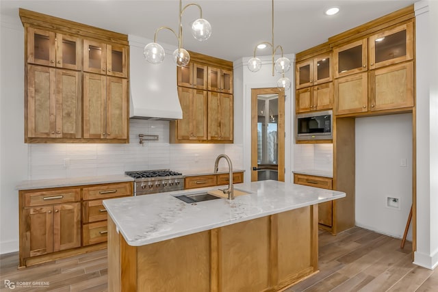 kitchen featuring sink, light stone counters, a kitchen island with sink, and built in microwave