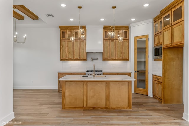 kitchen with stainless steel microwave, premium range hood, a kitchen island with sink, and tasteful backsplash