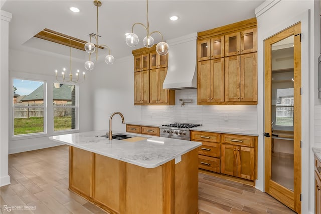 kitchen with custom exhaust hood, a kitchen island with sink, light stone countertops, sink, and stainless steel range oven