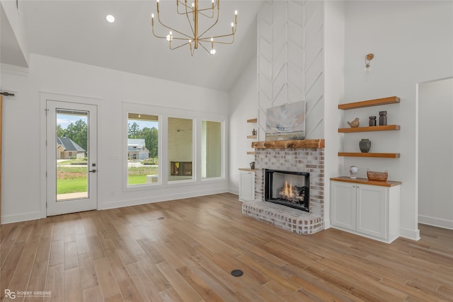 unfurnished living room featuring a brick fireplace, a notable chandelier, light hardwood / wood-style flooring, and high vaulted ceiling