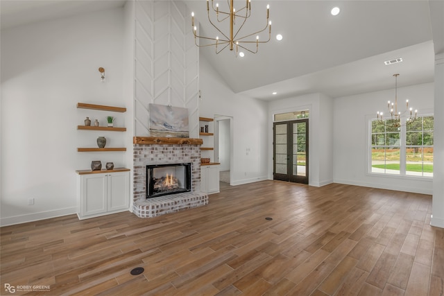 unfurnished living room with wood-type flooring, a fireplace, a chandelier, and high vaulted ceiling