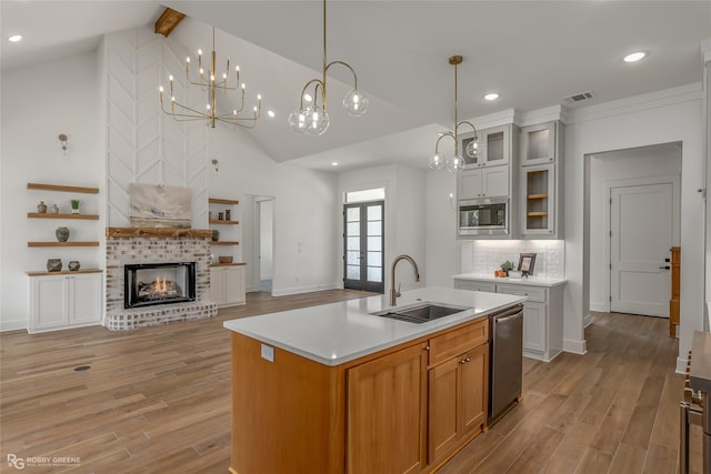 kitchen featuring sink, white cabinets, a kitchen island with sink, stainless steel appliances, and a brick fireplace