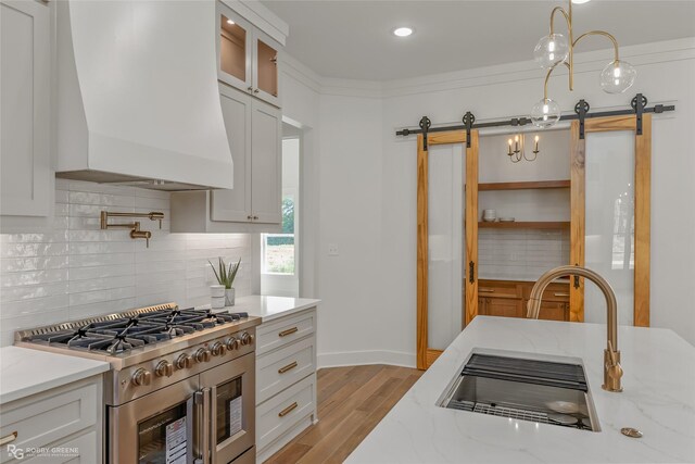 kitchen featuring an island with sink, a barn door, light wood-type flooring, stainless steel dishwasher, and sink