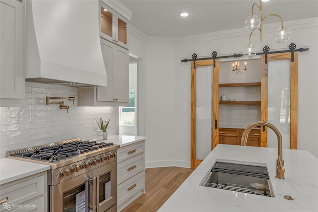 kitchen with stainless steel gas stove, custom exhaust hood, a barn door, and white cabinets