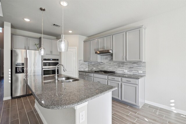 kitchen featuring sink, gray cabinets, an island with sink, tasteful backsplash, and stainless steel appliances