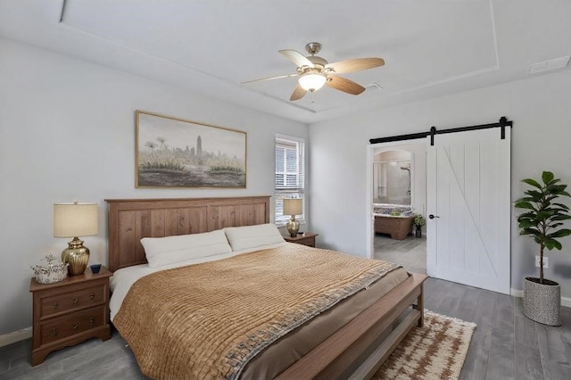 bedroom featuring ensuite bath, ceiling fan, a barn door, a tray ceiling, and dark hardwood / wood-style flooring