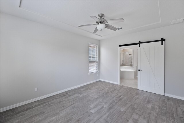 unfurnished bedroom with ceiling fan, a barn door, wood-type flooring, and connected bathroom