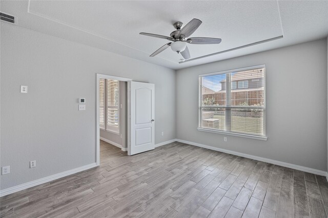 empty room featuring a textured ceiling, light wood-type flooring, ceiling fan, and a healthy amount of sunlight