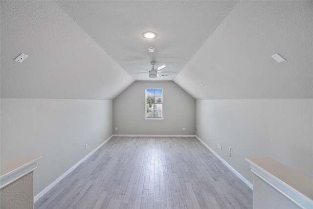 bonus room with light wood-type flooring, a textured ceiling, vaulted ceiling, and ceiling fan