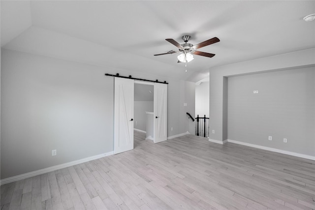 empty room with ceiling fan, a barn door, light hardwood / wood-style floors, and vaulted ceiling