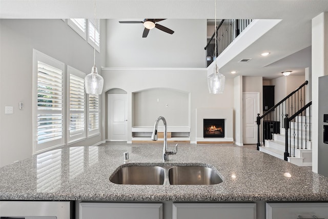 kitchen with decorative light fixtures, light stone countertops, sink, and a towering ceiling