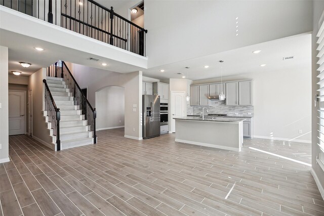 kitchen featuring stainless steel refrigerator with ice dispenser, decorative backsplash, a towering ceiling, an island with sink, and decorative light fixtures