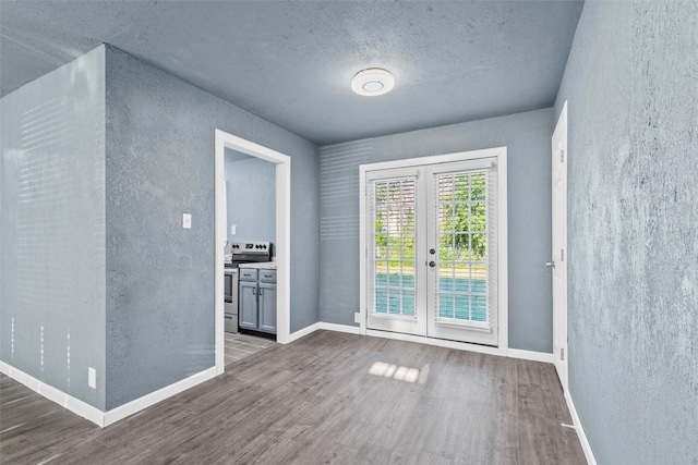 empty room featuring french doors, a textured ceiling, baseboards, and wood finished floors