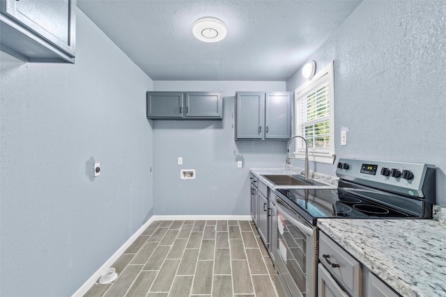 kitchen with baseboards, wood finish floors, stainless steel electric stove, gray cabinets, and a sink