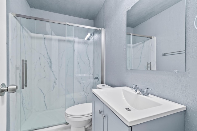 bathroom with vanity, toilet, a textured wall, and a marble finish shower