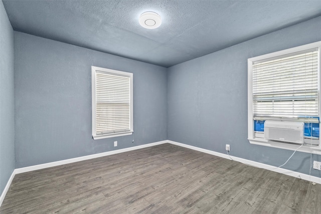 unfurnished room featuring cooling unit, wood finished floors, baseboards, and a textured ceiling