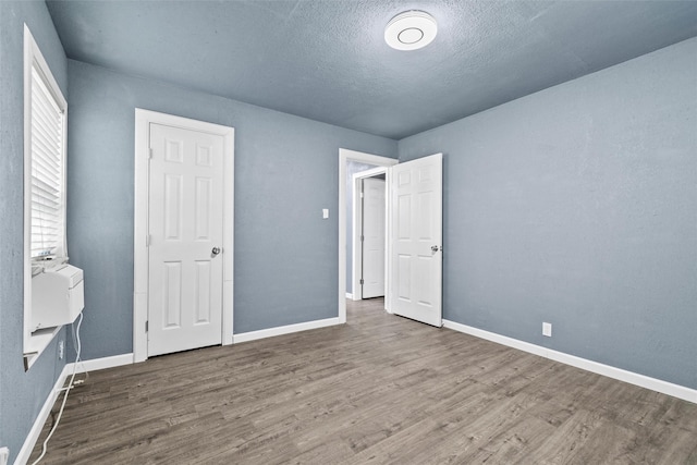 unfurnished bedroom featuring a textured ceiling, baseboards, and wood finished floors