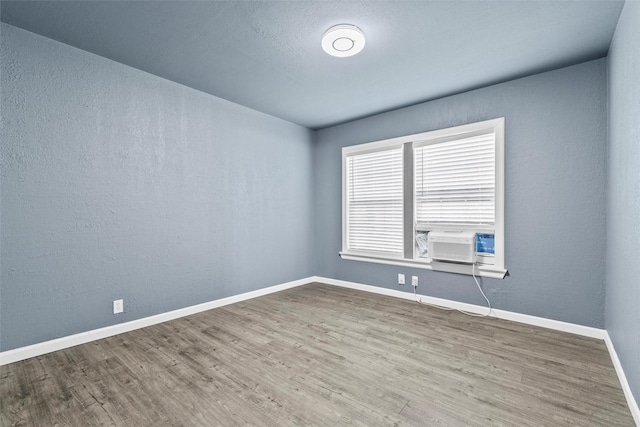 empty room featuring cooling unit, baseboards, wood finished floors, and a textured wall