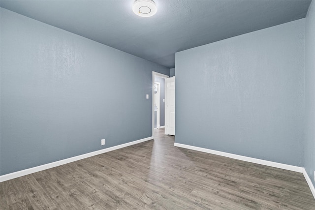 spare room with baseboards and wood finished floors