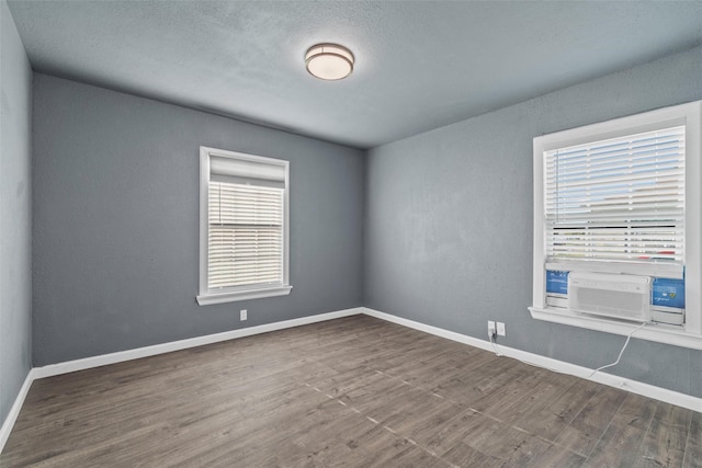 empty room featuring cooling unit, baseboards, and wood finished floors