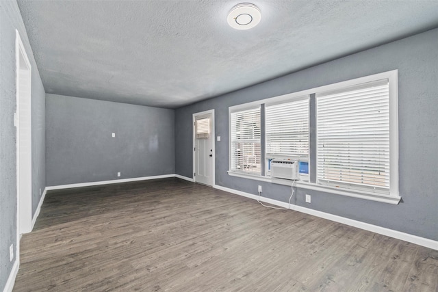 unfurnished room featuring cooling unit, a textured ceiling, baseboards, and wood finished floors