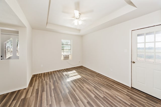 empty room with dark hardwood / wood-style flooring, a tray ceiling, and ceiling fan