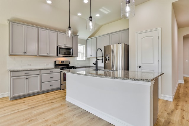 kitchen featuring appliances with stainless steel finishes, light wood-type flooring, an island with sink, and decorative backsplash