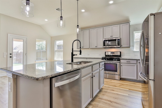 kitchen with light hardwood / wood-style flooring, appliances with stainless steel finishes, a center island with sink, backsplash, and sink