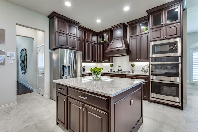 kitchen featuring decorative backsplash, custom range hood, light tile patterned floors, a center island, and stainless steel appliances