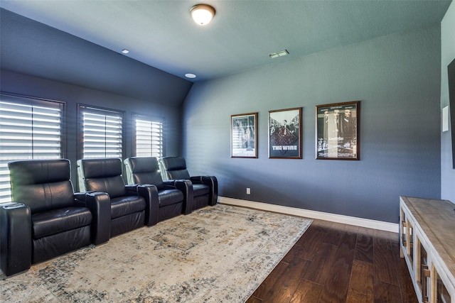 home theater room featuring lofted ceiling, visible vents, baseboards, and dark wood finished floors