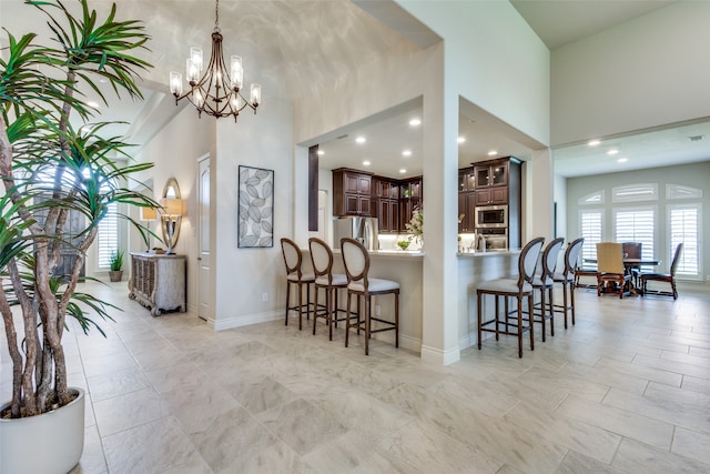 kitchen with a towering ceiling, hanging light fixtures, light tile patterned floors, an inviting chandelier, and stainless steel appliances