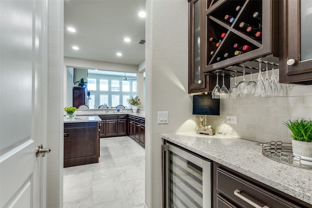 bar featuring light stone counters, backsplash, dark brown cabinets, and wine cooler