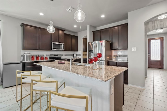 kitchen featuring a kitchen island with sink, sink, hanging light fixtures, and appliances with stainless steel finishes