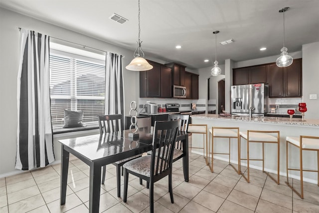 kitchen featuring dark brown cabinetry, hanging light fixtures, light stone counters, light tile patterned floors, and appliances with stainless steel finishes