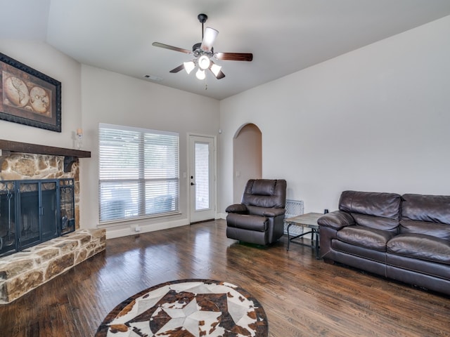 living room featuring ceiling fan, dark wood-type flooring, and a stone fireplace