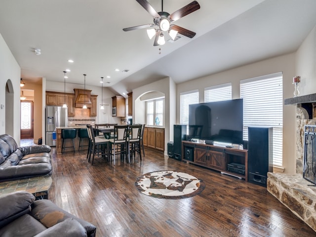 living room with ceiling fan, dark hardwood / wood-style floors, lofted ceiling, and a stone fireplace