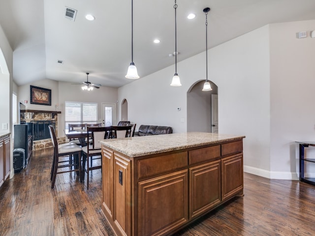 kitchen with dark wood-type flooring, a stone fireplace, hanging light fixtures, ceiling fan, and a center island