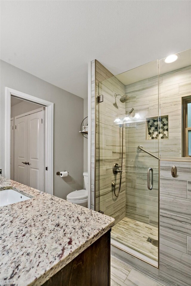 bathroom featuring a shower with shower door, vanity, and toilet